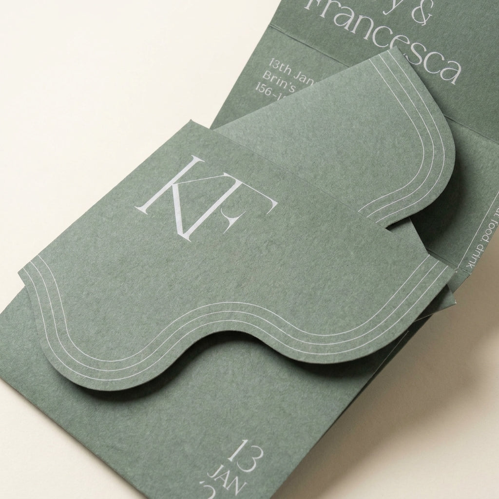Verdura sage green wedding invitation featuring a die-cut wavy edge, textured matte paper, and a white serif monogram.