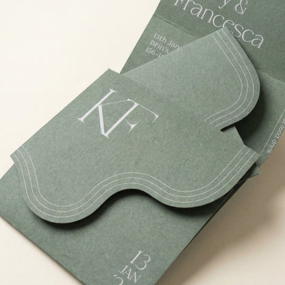 Verdura sage green wedding invitation featuring a die-cut wavy edge, textured matte paper, and a white serif monogram.