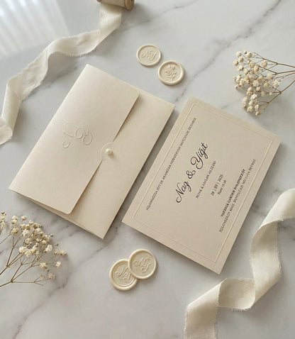 Celestina luxury wedding invitation on cream matte paper with embossed monogram, pearl detail, and cream wax seals.