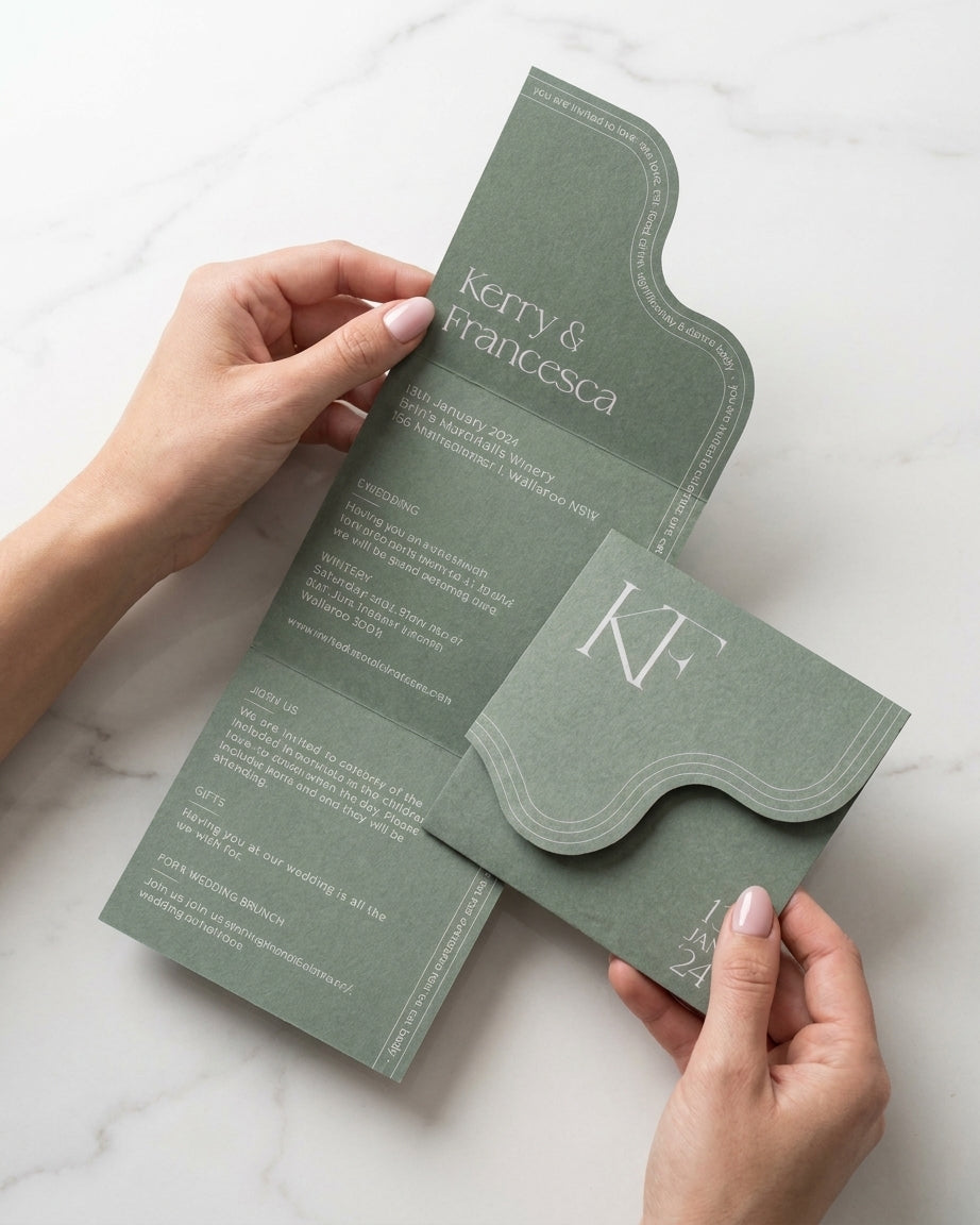 Hands hold the sage green Verdura wedding invitation featuring a unique wavy edge and elegant monogram on matte paper.