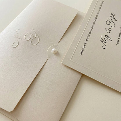 Celestina wedding invitation featuring a cream embossed monogram pocket with a pearl fastener and elegant calligraphy.